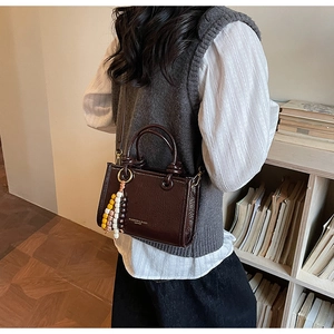 Detail view of coffee brown patent leather crossbody bag with colorful bead charm