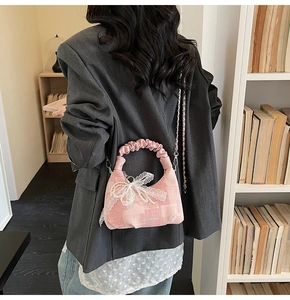 Detailed view of pink tweed dumpling bag with lace bow and pearl chain on a model