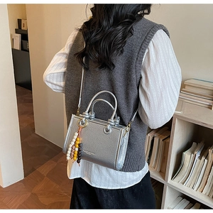 Detail view of silver mini crossbody bag with leather texture and wooden beaded charm