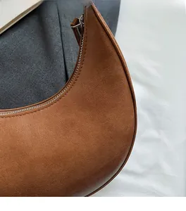Close-up of brown crescent bag showing fine leather texture and silver zipper detail