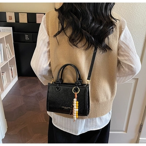 Detail of black glossy crossbody bag with beaded charm and leather text on a model