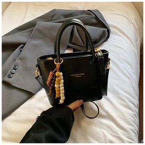 Detailansicht der schwarzen Handtasche mit goldenem Logo und buntem Perlenanhänger