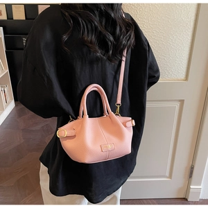 Détail du sac seau rose en cuir grainé avec poignée et plaque de logo dorée