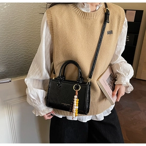 Close-up of black crossbody bag with pleated texture and colorful wooden bead charm