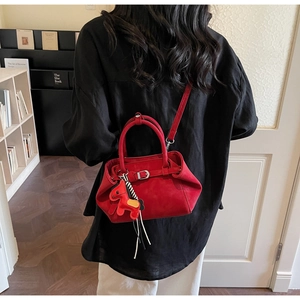 Detail showing red suede handbag with horse charm accessory and detachable shoulder strap