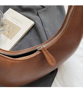 Detailed close-up of the smooth metal zipper and leather puller on a brown crescent bag