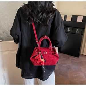 Detail of red suede handbag with wrap-around strap and horse charm worn by a model