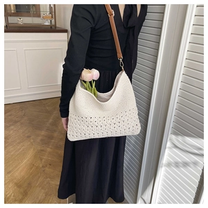 Detail of hand-woven straw shoulder bag featuring intricate hollow floral patterns and leather strap