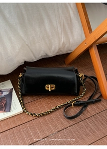 Detail of a black glossy rectangular shoulder bag with a golden geometric swivel lock