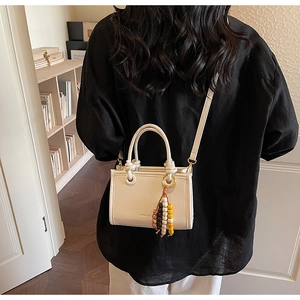 Detail view of cream crossbody bag with lychee grain texture and beaded tassel