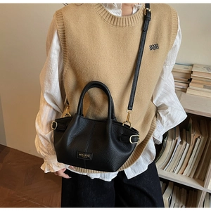 Détail du sac seau noir en cuir avec finitions dorées et logo sur une tenue décontractée