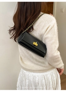 Close-up of a black rectangular chain bag with gold metal lock and leather strap