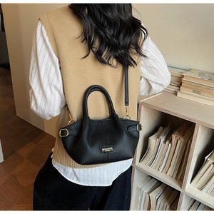 Détail du sac seau noir motif litchi avec logo doré et design plissé élégant