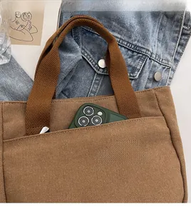 Gros plan de la poche extérieure du sac en toile beige contenant un smartphone