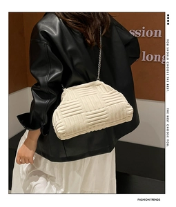 Détail du sac nuage tressé crème avec chaîne dorée fine porté à l'épaule par un mannequin