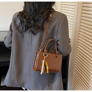 Detailed view of dark brown gloss crossbody bag with beaded tassel and knotted handle