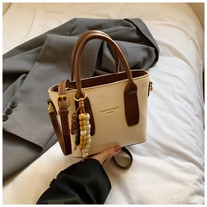 Detail der cremefarbenen Beuteltasche mit braunen Riemen und Anhänger aus Holzperlen