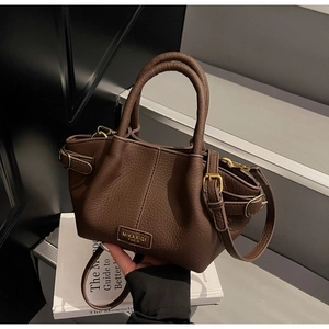 Détail d'un sac seau en cuir marron foncé à texture litchi avec plaque de marque dorée