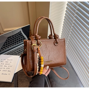 Detailed shot of retro brown leather handbag with knot handles and colorful wood bead charm