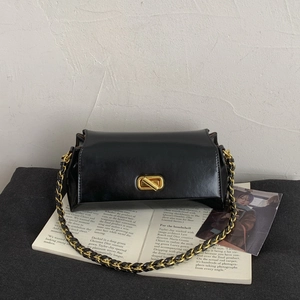 Detail of glossy black leather handbag featuring a gold turn-lock and chain strap