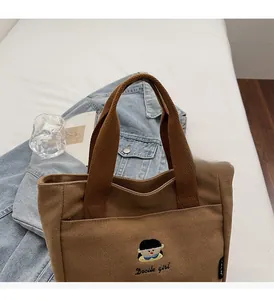 Détail du sac en toile marron avec broderie de fille et poignées renforcées