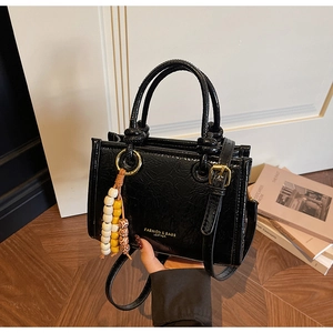 Detail of black crinkle patent leather crossbody bag with gold text and beaded charm