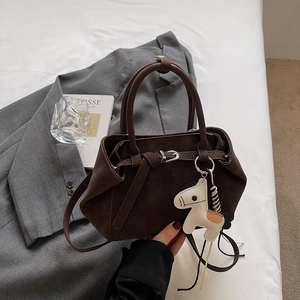 Detail of dark brown matte handbag with silver hardware and horse charm on a blazer