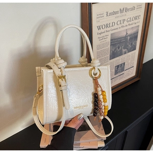 Detail of cream crinkled faux leather handbag with wooden bead tassel and double handles