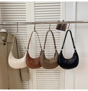 Minimalist crescent underarm bags in cream, tan, brown, and black hanging on a rack