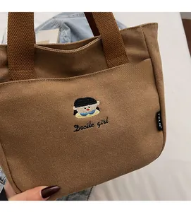 Vue détaillée du sac en toile marron avec broderie de fille et texte Docile girl