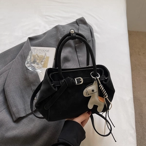 Detail of black chic handbag with horse charm and buckle straps on soft fabric