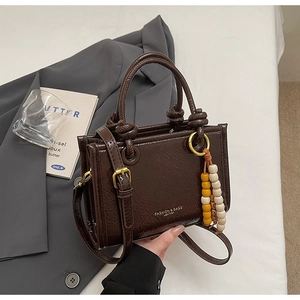 Detail of dark brown leather square bag with decorative knots and golden hardware buckle