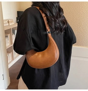 Brown leather crescent shoulder bag shown on model in a cozy minimalist home setting