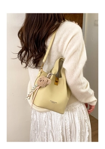 Sac seau chic en cuir crème à texture grainée avec charm ours porté par un mannequin