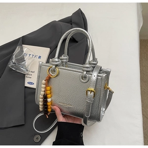 Detail of silver metallic textured crossbody bag with golden buckle and beaded charm