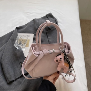 Detailed view of pink crossbody handbag with horse pendant and striped ribbon on white bed
