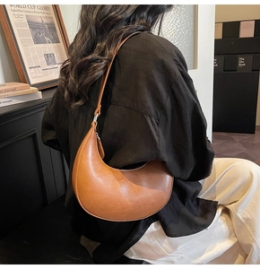 Brown leather crescent shoulder bag styled with vintage clothing in an artistic setting
