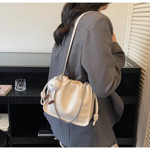 Détail d'un sac à main plissé blanc crème avec chaîne argentée et charm en peluche