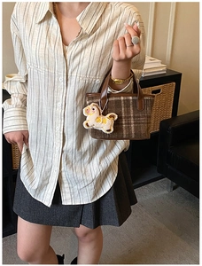 Close-up of brown plaid handbag with a white horse plush pendant in a lifestyle setting