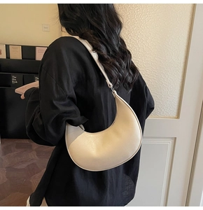 Close-up of a cream crescent hobo bag worn by a model in a casual setting