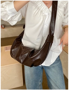 Detail of dark brown wrinkled croissant bag showing glossy texture and wide shoulder strap