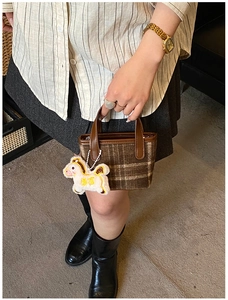 Detail of brown plaid tote bag featuring a leather handle and white plush horse charm