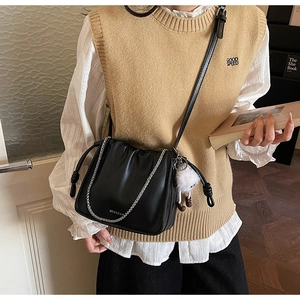 Détail du sac noir avec chaîne argentée, logo gravé et pendentif en peluche blanche