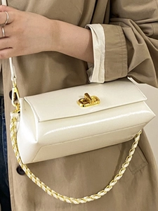 Minimalist beige crossbody bag with gold twist lock and woven chain strap on a model