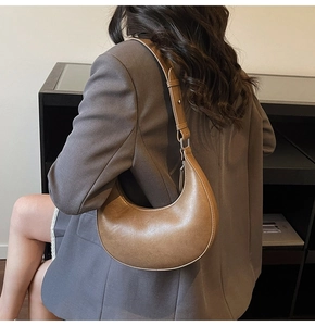 Close-up of a retro brown leather half-moon shoulder bag with fine texture and silver buckle