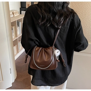 Détail du sac seau plissé marron foncé avec chaîne argentée et pompon blanc sur modèle