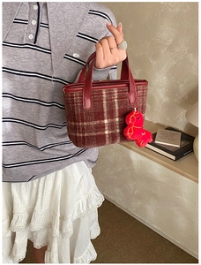 Detail of red plaid bucket bag with plush horse charm and leather handle on a textured fabric
