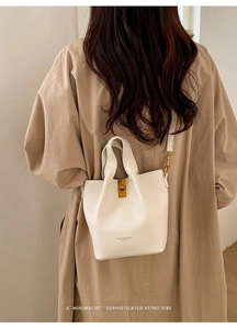 Gros plan du sac seau en cuir blanc avec fermoir doré sur un trench-coat kaki élégant