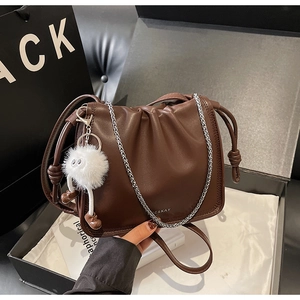 Détail d'un sac nuage plissé marron foncé avec chaîne argentée dans un coffret cadeau