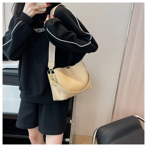 Detail view of beige leather bucket bag with gold clasp and stylish wide fabric strap